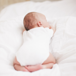 a baby dressed in white sleeping on their tummy