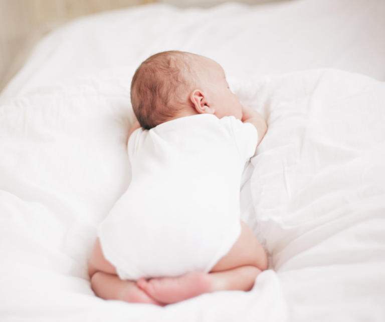 a baby dressed in white sleeping on their tummy