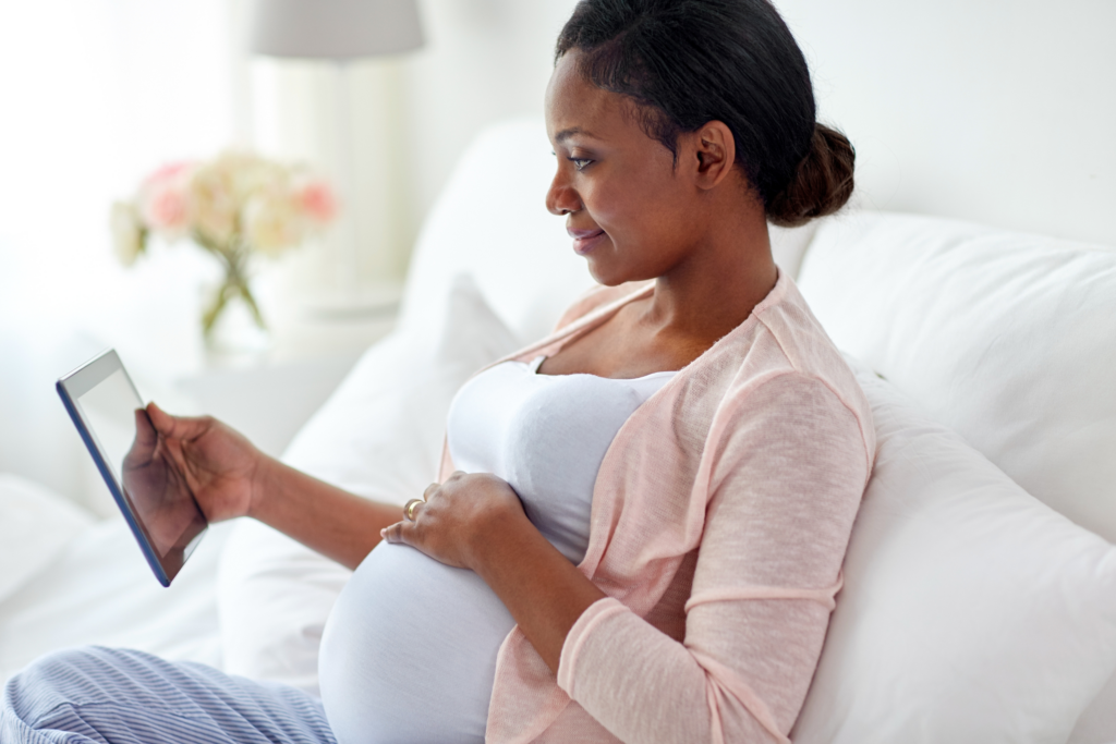 A dark-skined pregnant woman looking at a mirror.