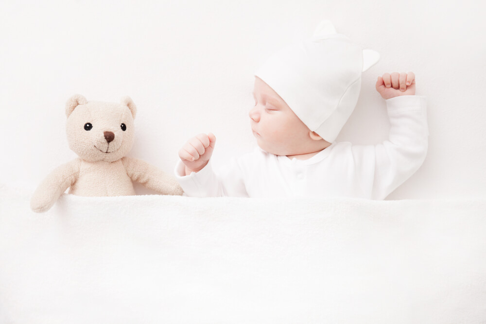 A baby dressed in white sleeping without mittens.